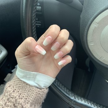 Dazzle Nails - Ombré nails - The image shows a person's left hand with long, natural, well-maintained nails, positioned near the steering wheel of a car. The person is wearing a beige knitted sweater and a white shirt cuff. The interior of the vehicle includes a black steering wheel and dashboard controls, with part of the instrument panel visible. - Nail Salons Near Me - Sandy, Oregon