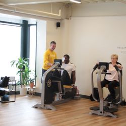 Osteostrong Lakewood - Two clients on the left are being coached through their session carefully,  & the client in the massage chair is enjoying compression boots.