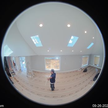 Speedy Gonzalez - First day protecting the floors - The image shows a spacious living room under construction, with a person standing in the center. The room has large windows and skylights allowing natural light, and the floor is covered with protective material. Construction tools and supplies are visible, indicating ongoing renovation work. - General Contractors Near Me