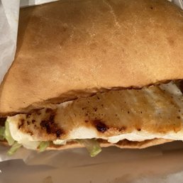 Spicy Crispy Chicken Sandwich - A grilled chicken sandwich with lettuce is inside a bun, partially wrapped in paper, on a tray or surface.