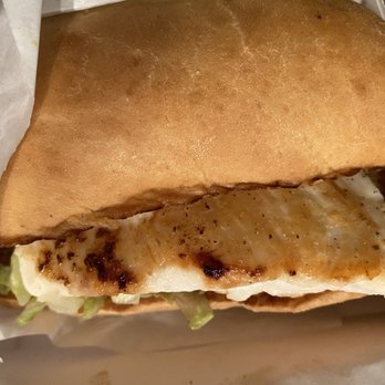 Culver's - Grilled chicken sandwich - A grilled chicken sandwich with lettuce is inside a bun, partially wrapped in paper, on a tray or surface. - Ice Cream & Frozen Yogurt Near Me - Jacksonville, Florida