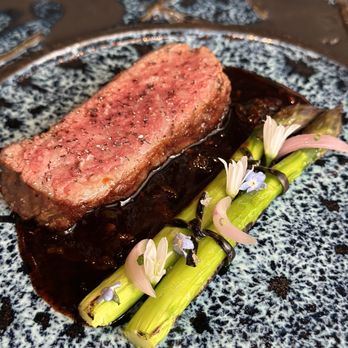 Aubergine - 32 day dry aged ribeye triple seared marinated in rock salt, sake & tamari w asparagus, chive & onion blossoms w/wagyu xo sauce & beef jus - New American Near Me - Carmel, California