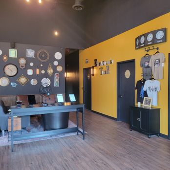 Escapology - The image shows the reception area of an escape room business with a yellow wall, clocks, and merchandise for sale, including T-shirts. - Escape Games Near Me - Tempe, Arizona
