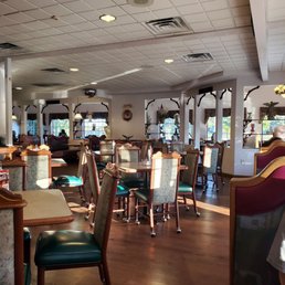 Restaurant - A family restaurant interior with multiple tables and chairs, windows with curtains, and some patrons seated, illuminated by natural sunlight.