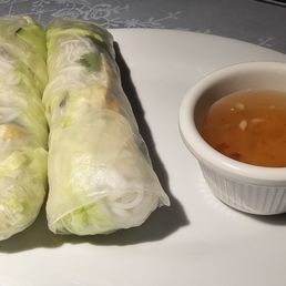Spring Roll - Two Vietnamese spring rolls wrapped in translucent rice paper are served with a small bowl of dipping sauce on a white plate.