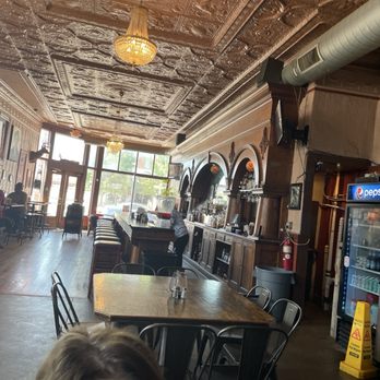 Lindberg's Tavern - A spacious tavern features a decorative tin ceiling, a bar with arched mirrors, and seating near large front windows, with patrons and a staff member present. - Bars Near Me - Springfield, Missouri