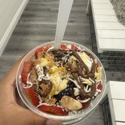 Acaí bowl: tropical and mange base with strawberries, blueberries, almonds coconut, Nutella drizzle, and cinnamon powder