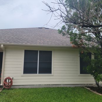 Diamond Select Roofing - A residential house features beige siding, two windows with dark blinds, and a tree in the front yard with some leaves. - Roofing Near Me - Pflugerville, Texas