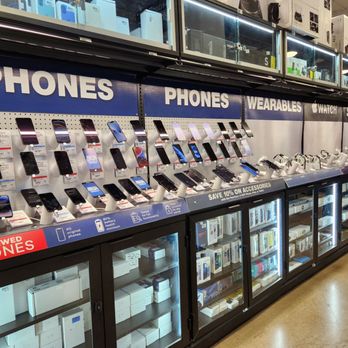 Micro Center - A retail store shelf showcases multiple smartphones on stands, with signage indicating phone categories and discounts, along with glass cabinets containing boxed accessories. - Computers Near Me - Tustin, California