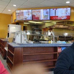 The menu (andy finger) - Three digital menu screens show food and drink options in a casual dining setting, with a counter and kitchen area below.