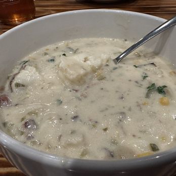 Backyard Brewery - Haddock chowder,  yum! - A large white bowl contains haddock chowder with a creamy texture, pieces of fish, corn, and herbs, on a wooden table. - Breweries Near Me - Manchester, New Hampshire
