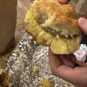Inxpot - Horrible biscuit, takes like baking soda. Supposed to be a bacon biscuit with no cheese. It's a sausage biscuit smothered in pepper jack. - A person holds a large breakfast biscuit with visible eggs, sausage, and melted cheese, with foil and food remnants on the table. - Coffee & Tea Near Me - Keystone, Colorado