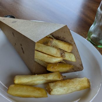 Mister Pio - French fries are served in a paper cone on a white plate, with some fries spilled onto the plate. A glass bottle is visible in the background. - Peruvian Near Me - Phoenix, Arizona