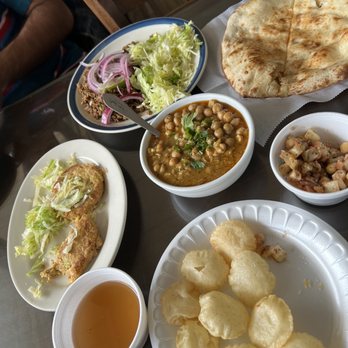 Mughal's Oasis - a variety of indian food - A table displays Indian and Pakistani cuisine with naan bread, chickpea curry, salad, fried snacks, and a cup of tea, typical of Mughal's Oasis. - Pakistani Near Me - Springfield, Virginia