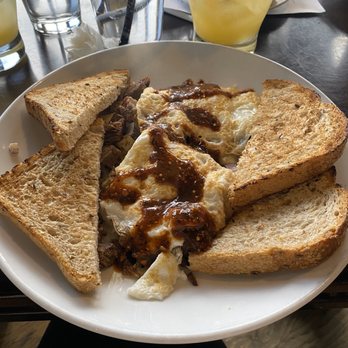 Uptown Kitchen - Brisket hash - A breakfast plate featuring toast, fried eggs with sauce, and cooked meat, with drinks including water, juice, and a yellow beverage on a table. - New American Near Me - Granger, Indiana