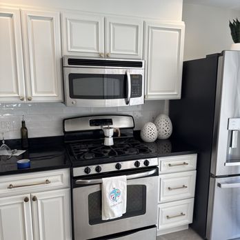 Mk Renovation - Kitchen featuring white cabinetry, a stainless steel microwave and stove, and decorative ceramic vases on the black countertop. - Painters Near Me - Somerville, Massachusetts