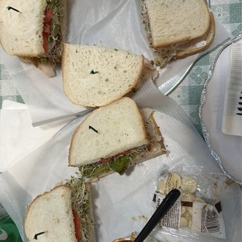a.k.a. Friscos - Alcatraz Sandwich and 12 oz. Large Spicy Beef Chilichili - A metal tray contains five sandwich halves made with white bread, filled with sprouts, tomato, and turkey, arranged around a cup of chili topped with shredded cheese. The tray is lined with white paper and placed on a green checkered tablecloth, with a small packet of crackers and a plastic water bottle nearby. - American Near Me - Frederick, Maryland