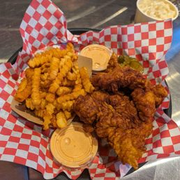 Tenders hot - A basket of fried chicken tenders and crinkle-cut fries with dipping sauces, served on checkered paper at a restaurant.
