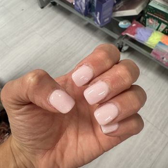The Nail Logic - A hand with neatly manicured, light pink, glossy nails is shown in front of a store shelf with various products. - Nail Salons Near Me - Gilbert, Arizona