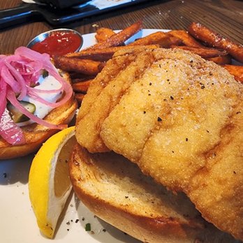Burtons Grill & Bar - Fried Fish Sandwich - served with pickled onions, pickles, tartar sauce on a brioche roll. The sweet potato fries were 10/10 - New American Near Me - Plantation, Florida