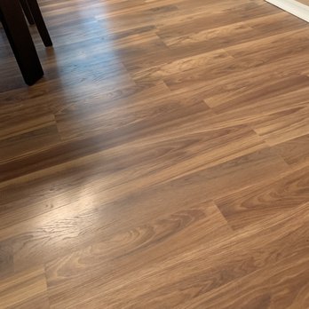 LL Flooring - Garner - Fairfield County Hickory laminate. - Interior wooden flooring with a floor vent and part of a dark table leg visible in the corner. - Flooring Near Me - Garner, North Carolina