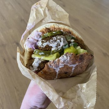 Nura - a person holding a sandwich wrapped in wax paper - Mediterranean Near Me - Portland, Maine