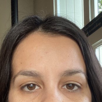 Eyebrow Masters - A woman with brown eyes and dark hair is indoors, with a window and a television in the background. - Eyebrow Services Near Me - Turlock, California