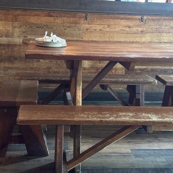 Bakersfield Mass Ave - Inside seating - A rustic wooden table with a plate holding napkins is positioned against a wooden-paneled wall in a dining area. - Bars Near Me - Indianapolis, Indiana