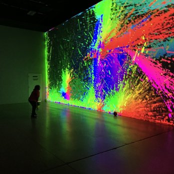 Electric Playhouse - A person observes a vibrant digital art installation with bright, multicolored patterns projected on a wall in a dark indoor space. - Party & Event Planning Near Me - Albuquerque, New Mexico