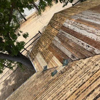 Waterproof Roofing - Before - A wooden deck made of weathered planks is shown outdoors, with a tree and a metal railing nearby. - Roofing Near Me - Clovis, California