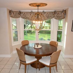 Interiors by Thalia - Roman shades in a casual dining room create an open airy experience with an eclectic chandelier.