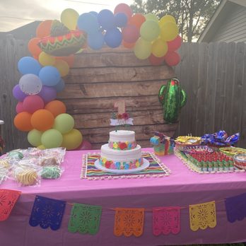 Allegretti's Bakery - Fiesta birthday theme - A birthday celebration features a two-tiered cake, colorful balloons, and party favors on a pink tablecloth in a backyard setting. - Bakeries Near Me - Norridge, Illinois