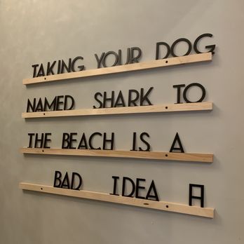 Storm Coffee - a sign that says taking your dog named shark to the beach is a bad idea - The image shows a decorative wall sign with black letters attached to horizontal wooden slats. The sign displays a humorous quote about dogs and the beach, reading: 'TAKING YOUR DOG NAMED SHARK TO THE BEACH IS A BAD IDEA.' The sign is mounted on a plain, light-colored wall, and the letters are arranged in four lines with spacing between the slats. - Coffee & Tea Near Me - Turner, Oregon