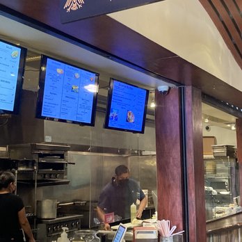 Mexicana - Spot - Inside Mexicana Taqueria, staff are preparing food behind a glass partition, with digital menu screens above the counter. - Mexican Near Me - Berkeley, California