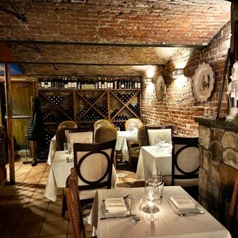 Ristorante Euno - The image shows a restaurant interior with exposed brick walls and a low, brick ceiling. There are wine racks filled with bottles against the back wall. Several tables are set with white tablecloths, glassware, and silverware, ready for diners. The lighting is warm, and decorative plates are mounted on the walls. The overall ambiance appears intimate and suitable for fine dining. - Italian Near Me - Boston, Massachusetts
