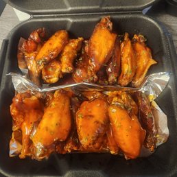 Valley sauce on top, honey hot on bottom - Chicken wings coated in barbecue sauce are arranged in a black takeout container with foil lining, garnished with chopped herbs.