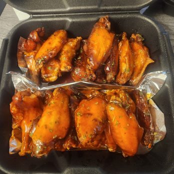 Valley Wings - Valley sauce on top, honey hot on bottom - Chicken wings coated in barbecue sauce are arranged in a black takeout container with foil lining, garnished with chopped herbs. - Chicken Wings Near Me - Phoenix, Arizona