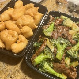 2 Piece Spring Rolls - A photo shows two black takeout containers with fried dough balls and beef with broccoli, placed on a kitchen countertop.