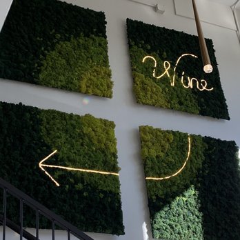 Trellis Wine Bar - a wall of moss - Four moss panels with neon signs and arrows are mounted on a white wall, creating a modern decorative display. - Wine Bars Near Me - Denver, Colorado
