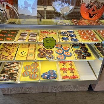 Allegretti's Bakery - Iced specialty cookies - A glass display case at Allegretti's Bakery showcases Halloween-themed decorated cookies, including pumpkins, pandas, and sports designs, with a pumpkin decoration on top. - Bakeries Near Me - Norridge, Illinois