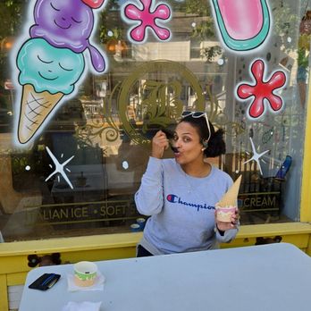 Bozerinos - A woman in a Champion sweatshirt holds an ice cream cone outside an ice cream shop decorated with cartoon ice cream and milkshake illustrations. - Ice Cream & Frozen Yogurt Near Me - Cold Spring, New York