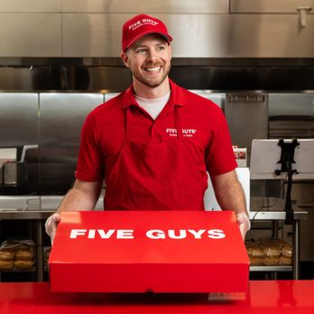 Five Guys - A Five Guys employee holds the red Five Guys catering box at the counter. - Burgers Near Me - Bradley, Illinois