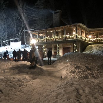 Johnny Seesaw's - The view from the hut. - People are gathered outside a lodge decorated with string lights and wreaths, surrounded by snow at night. - American Near Me - Peru, Vermont
