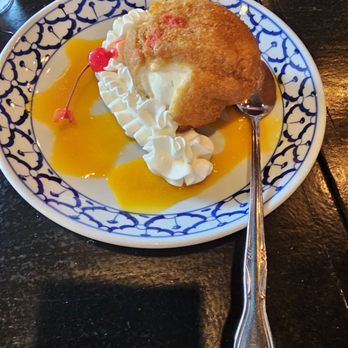 Sabay - A slice of cake with whipped cream, a cherry, and yellow sauce on a patterned plate, placed on a dark wooden table. - Thai Near Me - Elmhurst, New York