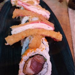 Yakuza - YAKUZA Salmón, atún, merluza tempura, queso crema, cebollino, envuelto en masago con salsa dinamita y tope de langostino y surimi tempura.