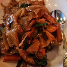 Pad See Ew - A bowl containing stir-fried noodles with vegetables such as carrots, green onions, and mushrooms, along with seafood like shrimp.