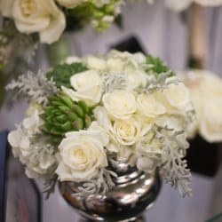 Elegant white roses, silvery grey dusty miller, fragrant white freesia and unique succulents create a charming centerpiece.