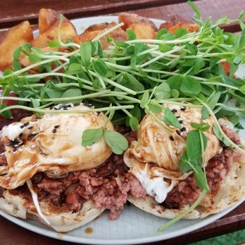 HeadQuarters - HQ Benedict (protein = sausage) - A dish featuring microgreens, ground meat, poached eggs, and fried potatoes served on a white plate on a wooden table. - Cafes Near Me - Ottawa, Ontario