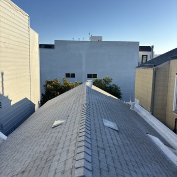Precise Roofing - A rooftop with two skylights is seen from above, with neighboring buildings and trees in the background under a clear sky. - Roofing Near Me - Walnut Creek, California
