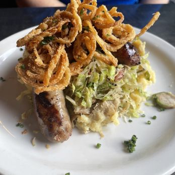 Not Your Average Joe's - Reston - Das Drunken Bratwurst Feast. Comes with bratwurst over a brussels sprout slaw over mashed garlic potatoes, topped by crispy onion rounds. - New American Near Me - Reston, Virginia Not Your Average Joe's - Reston - Das Drunken Bratwurst Feast. Comes with bratwurst over a brussels sprout slaw over mashed garlic potatoes, topped by crispy onion rounds. - New American Near Me - Reston, Virginia